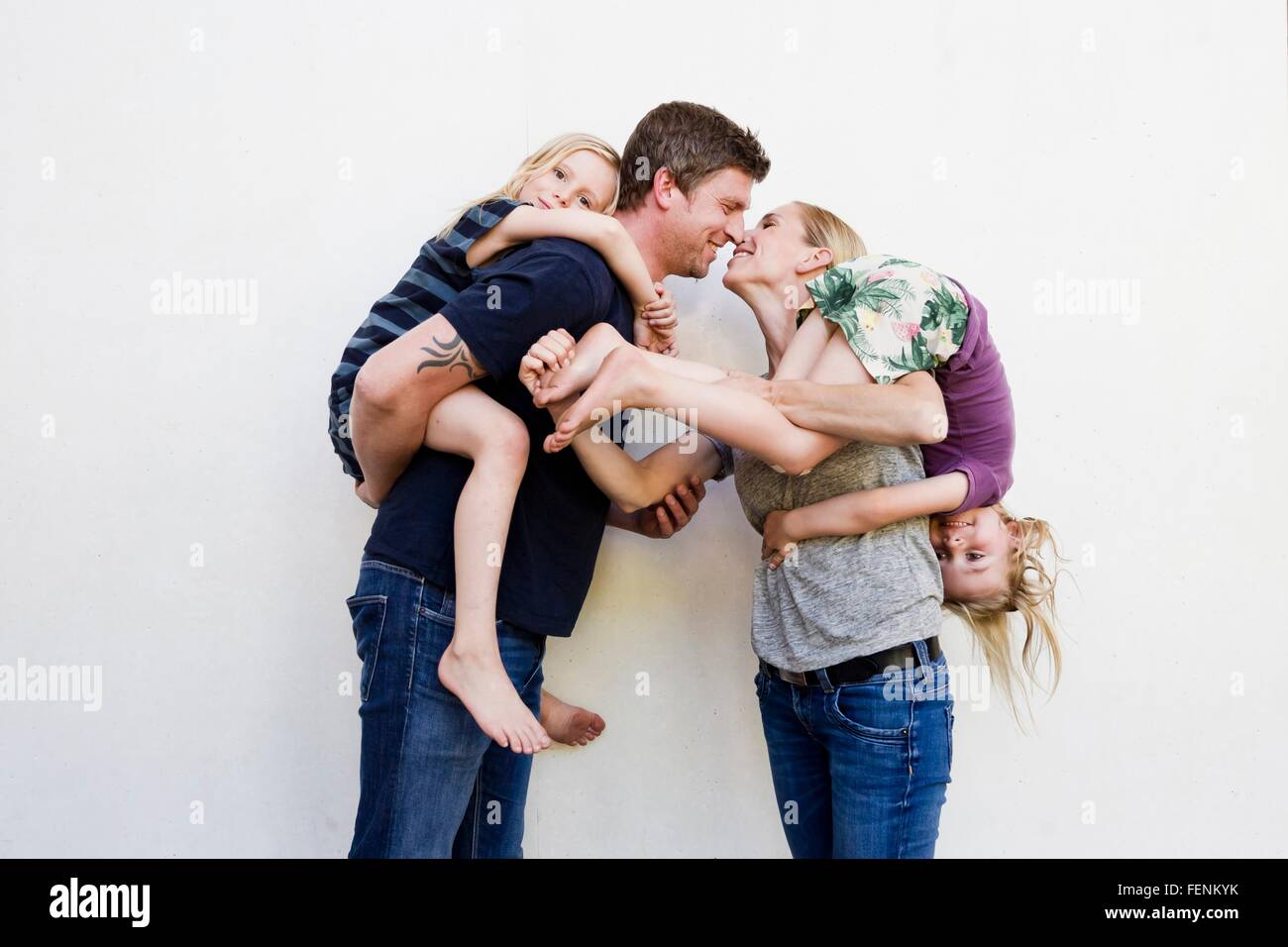 Portrait de parents transportant deux jeunes filles en face de mur blanc Banque D'Images