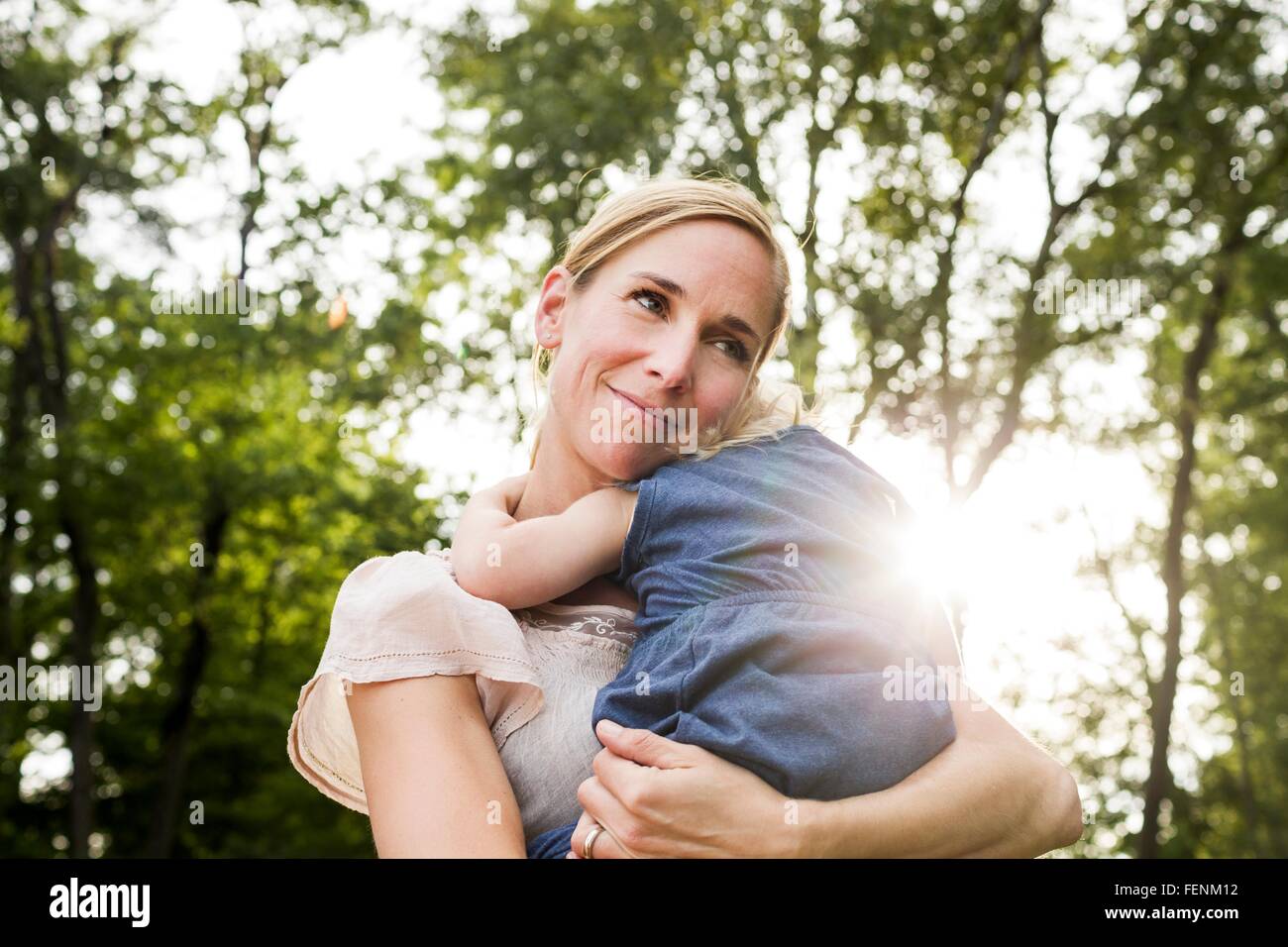 Mid adult woman carrying toddler daughter in sunlit park Banque D'Images