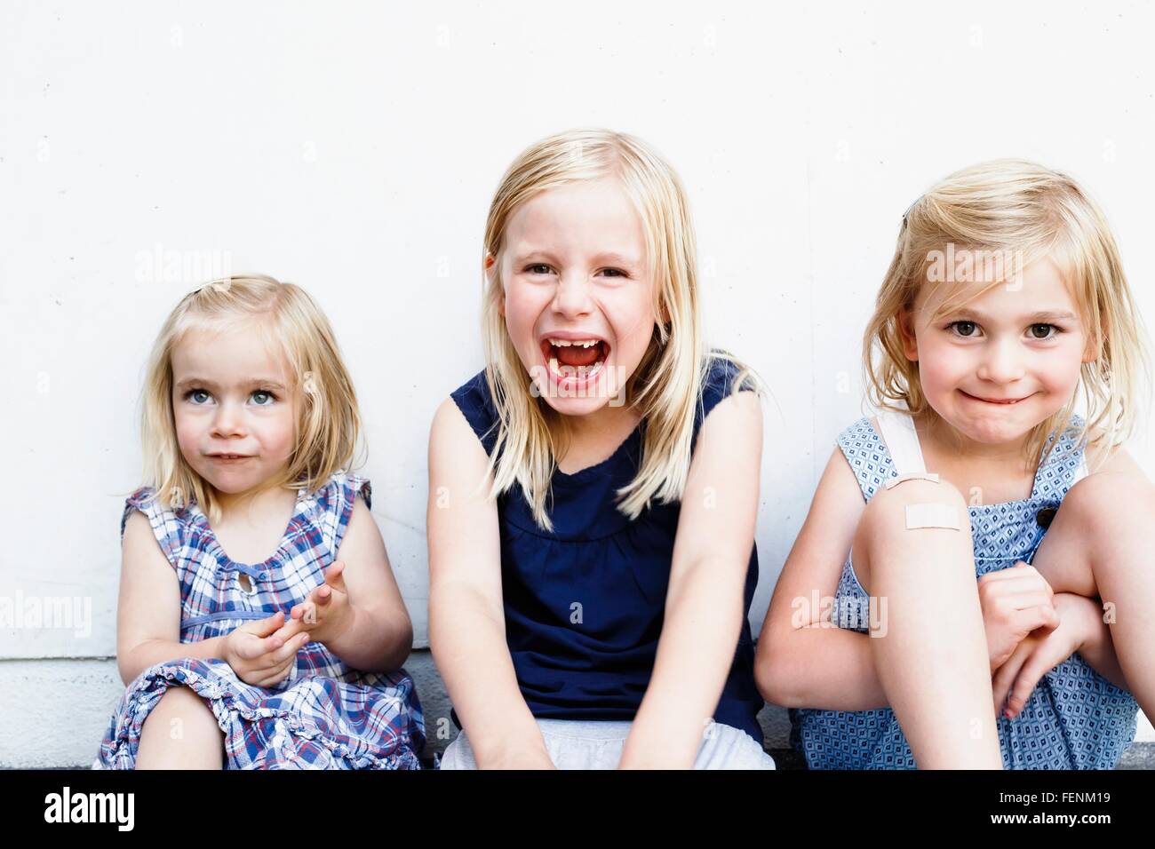 Portrait de trois jeunes sœurs assis en face de mur blanc Banque D'Images