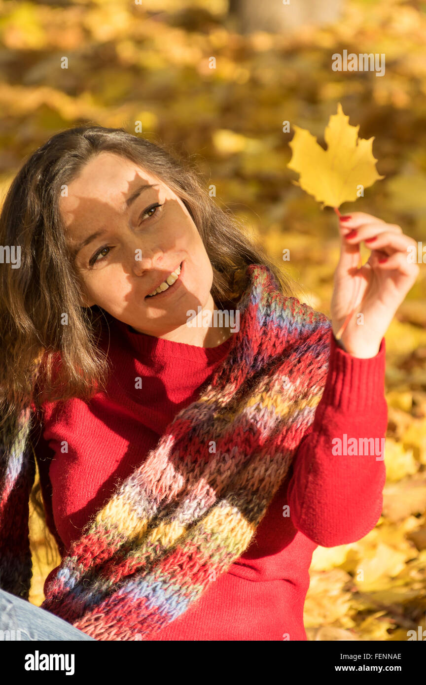 Femme aux cheveux brun à jaune automne forêt tenant une feuille d'érable avec ombre sur le visage Banque D'Images