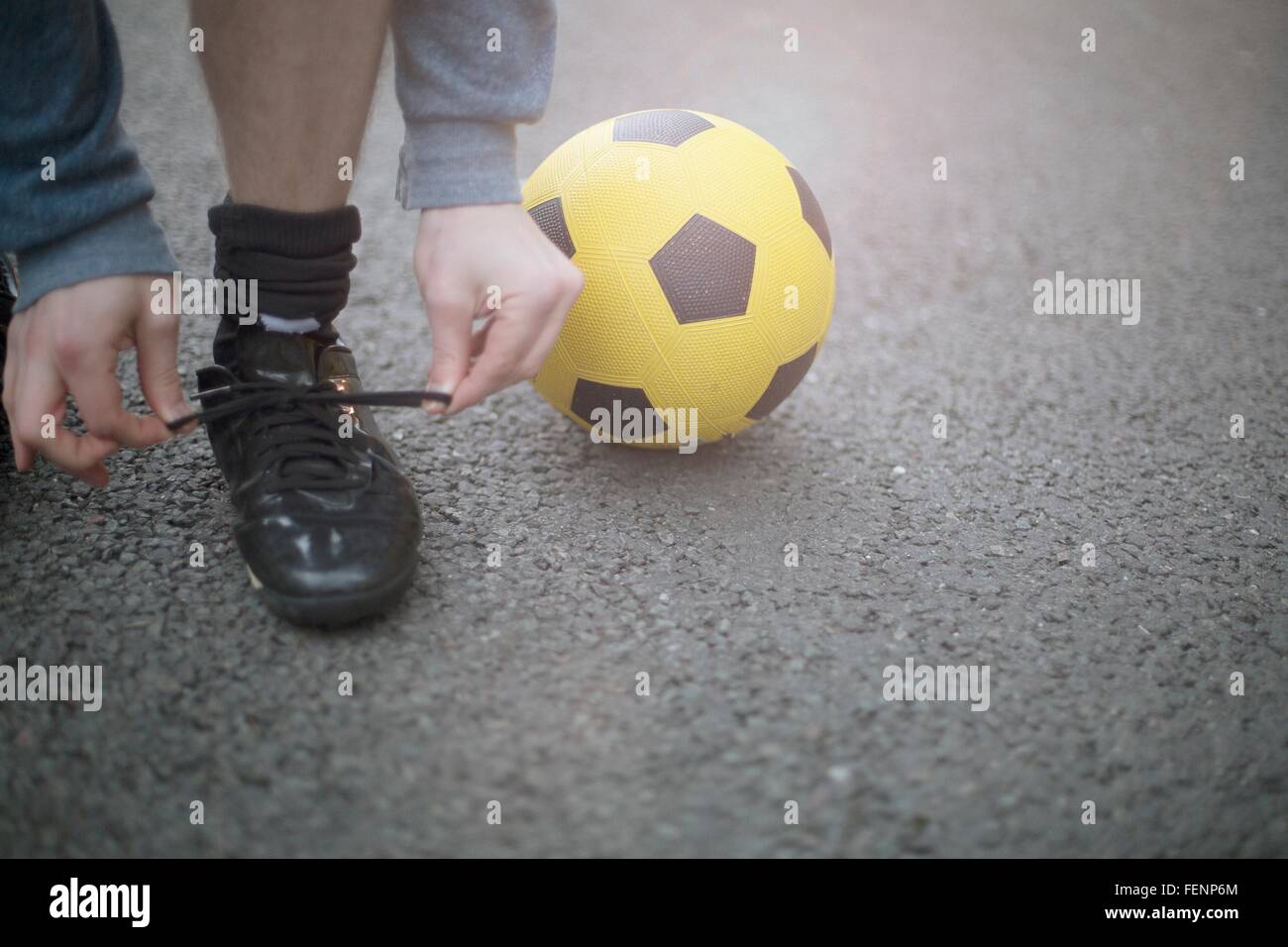Jeune homme attacher ses lacets, football à côté de lui, low section Banque D'Images