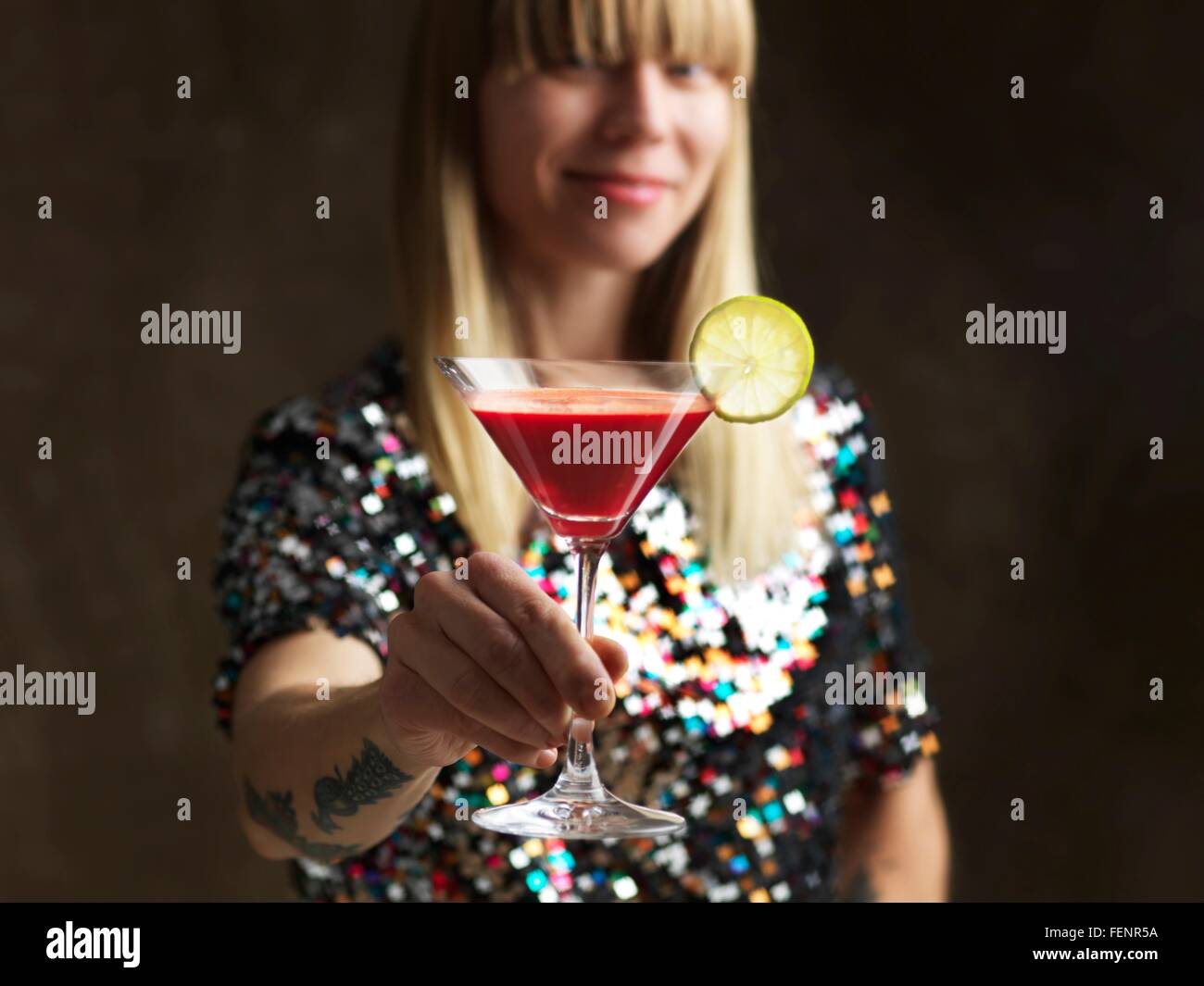 Mid adult woman holding jus cru dans verre à cocktail garni d'une tranche de lime smiling at camera Banque D'Images