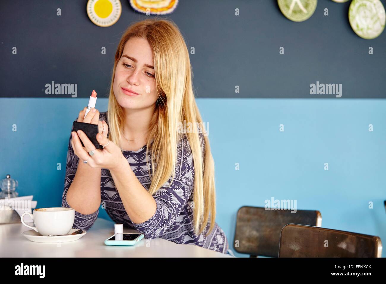 Jeune femme seule, en appliquant le rouge à lèvres cafe Banque D'Images