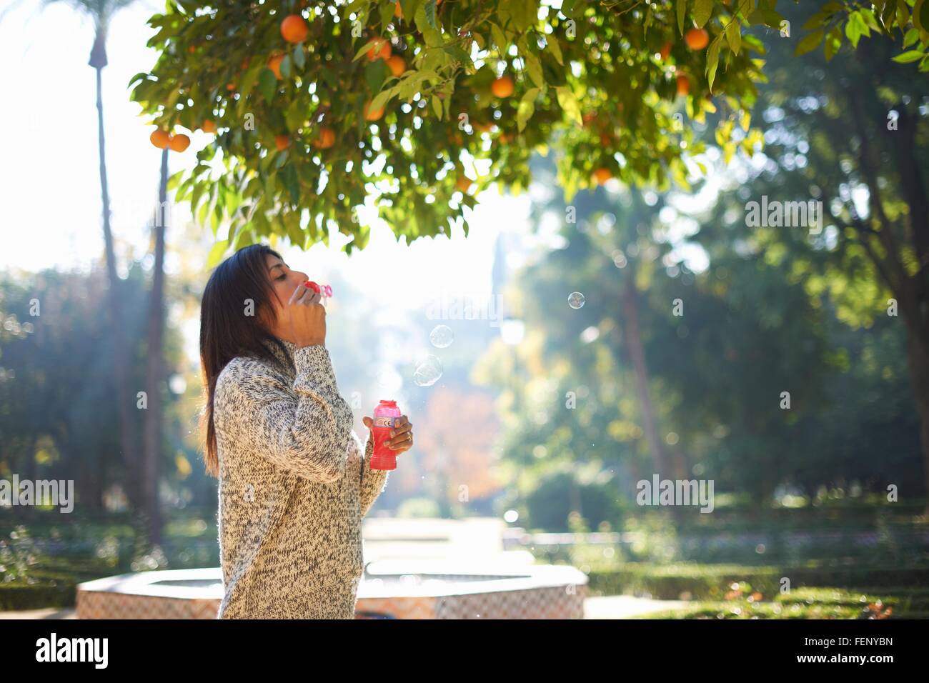 Vue de côté mature woman blowing bubbles en vertu de l'oranger, Séville, Espagne Banque D'Images