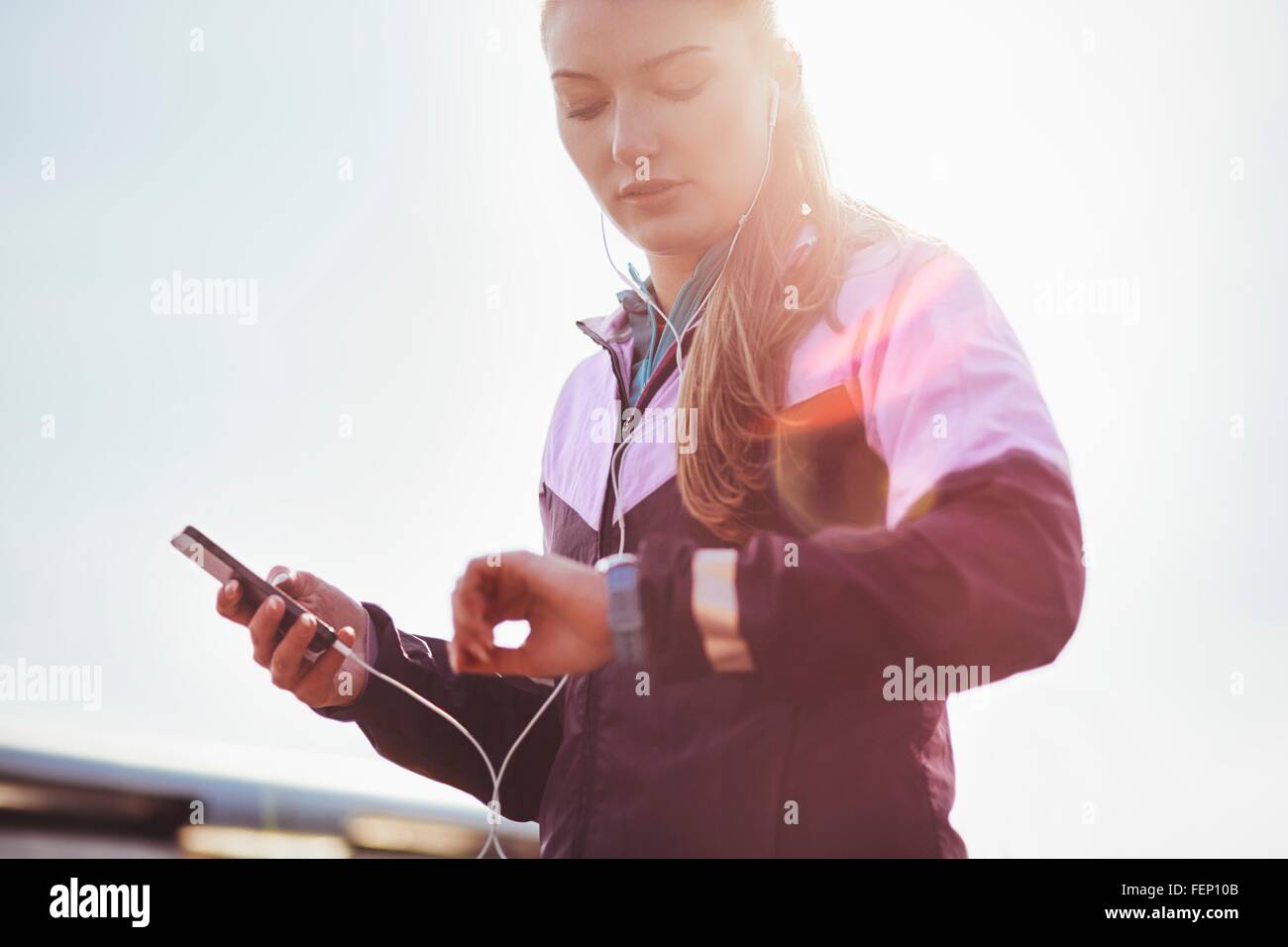 Mid adult female runner wearing earphones contrôle de temps sur smartwatch Banque D'Images