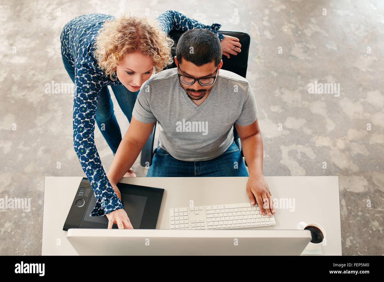 Vue de dessus coup de jeune homme assis à son bureau travaillant sur pc et tablette graphique numérique avec femme pointant sur moniteur. Homme gr Banque D'Images