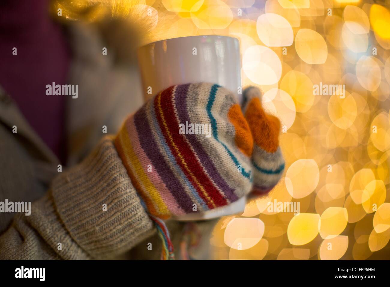 Close up of woman holding hands wearing mittens boisson chaude en face de lumières de Noël Banque D'Images