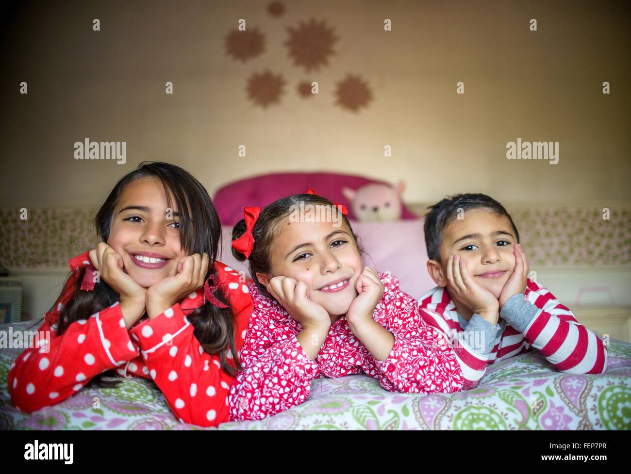 Enfants vêtus de pyjamas couché sur fronts sur menton lit dans les mains à  la caméra en souriant Photo Stock - Alamy