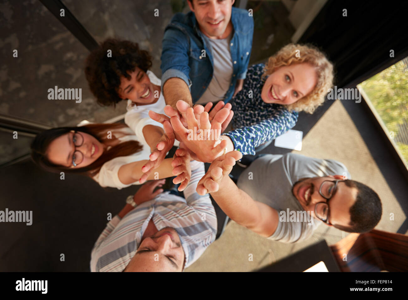 Vue de dessus de l'équipe de professionnels et on subit donc élevé à la caméra en souriant. Les hommes et les femmes faisant un tas de mains dans Banque D'Images