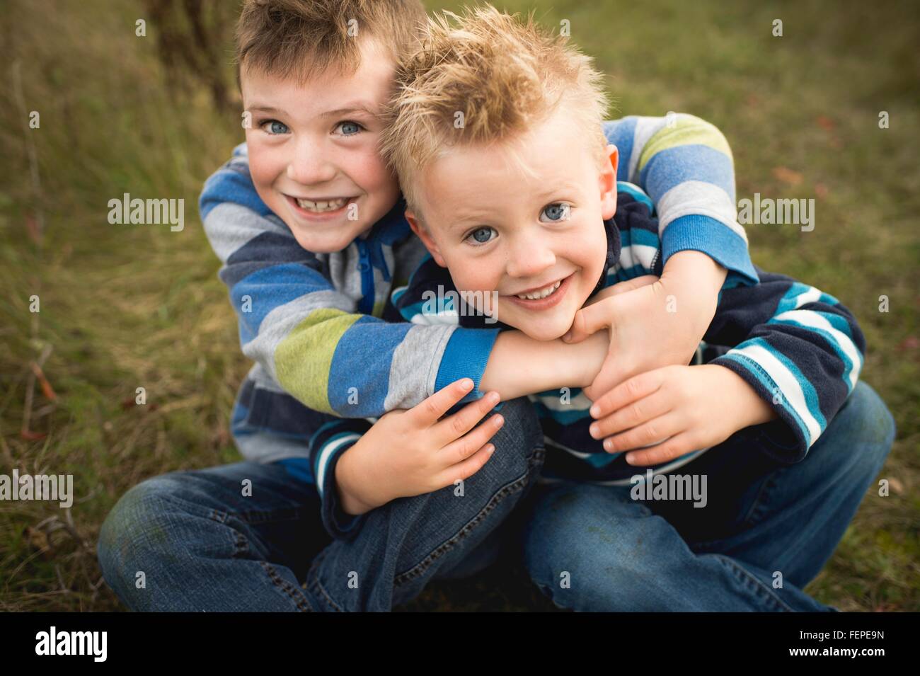 Portrait de garçons assis sur l'herbe s'étreindre, looking at camera smiling Banque D'Images