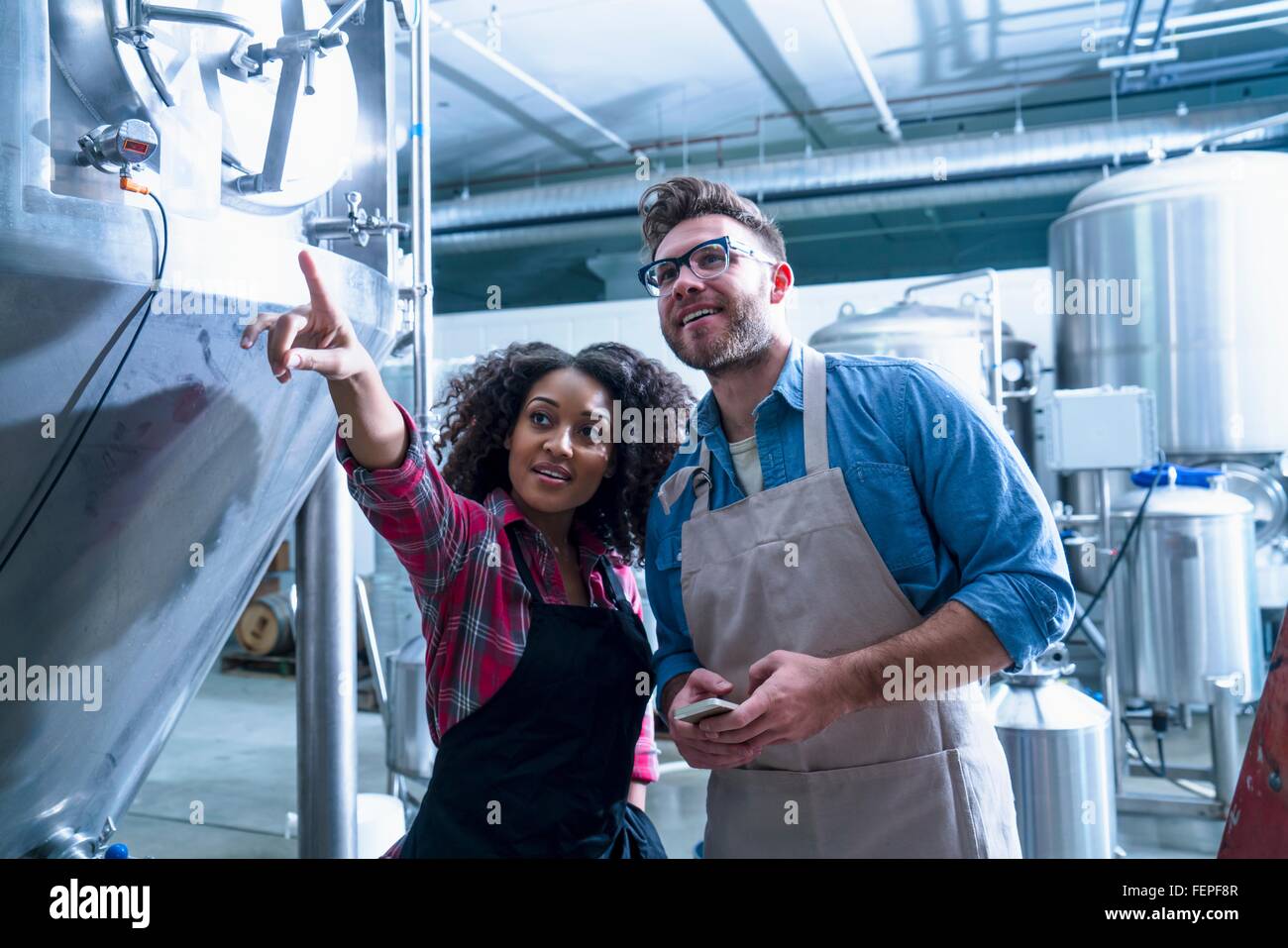 Collègues de brasserie par fermentation réservoir conique, pointant à up smiling Banque D'Images