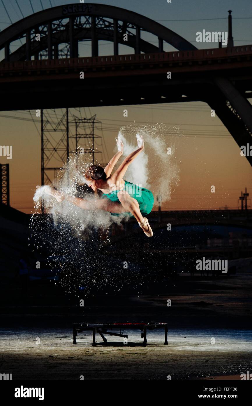 Ballerine femme sautant tout en libérant en poudre explosion au-dessus de trampoline au coucher du soleil, Los Angeles, USA Banque D'Images