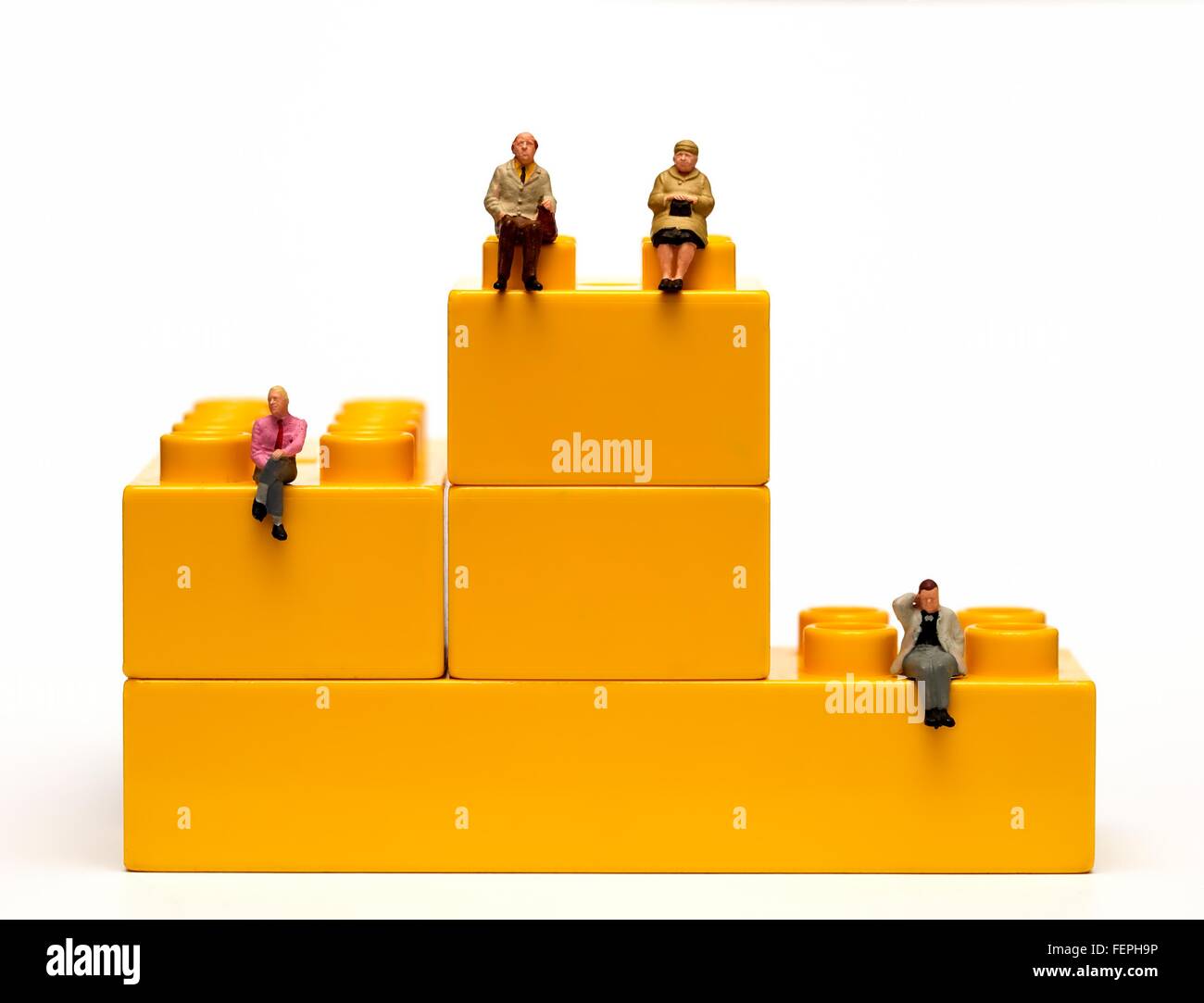 Une figurine miniature couple pension et 2 hommes assis sur des briques en plastique jaune d'enclenchement 1er 2e troisième concept pension Banque D'Images