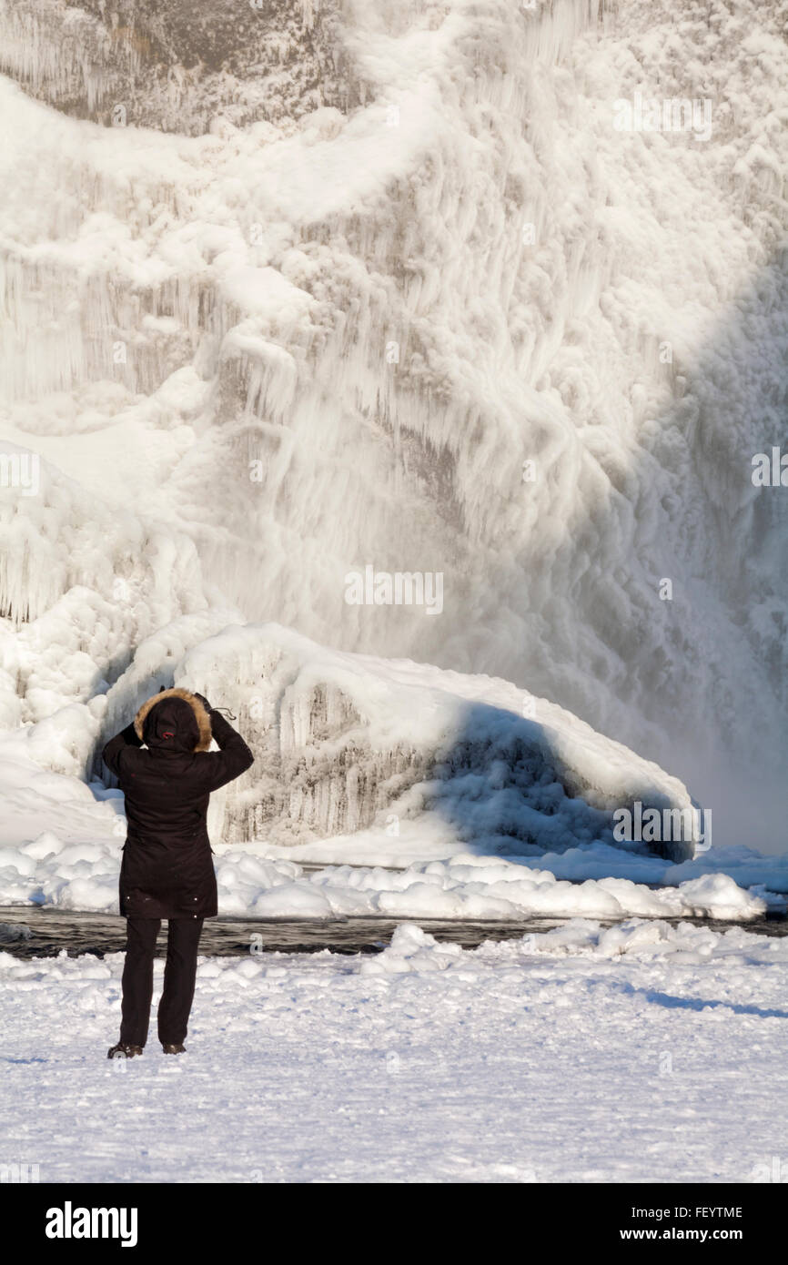 Jeune Femme prenant une photographie à Skogafoss Waterfall in winter wonderland avec l'eau gelée et de glaçons l'Islande en Janvier Banque D'Images