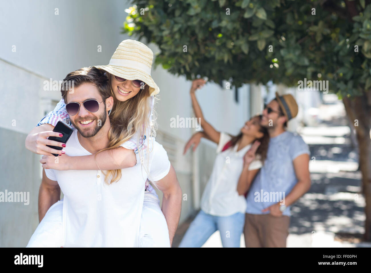Hip man giving piggy back pour son amie et prendre selfies Banque D'Images