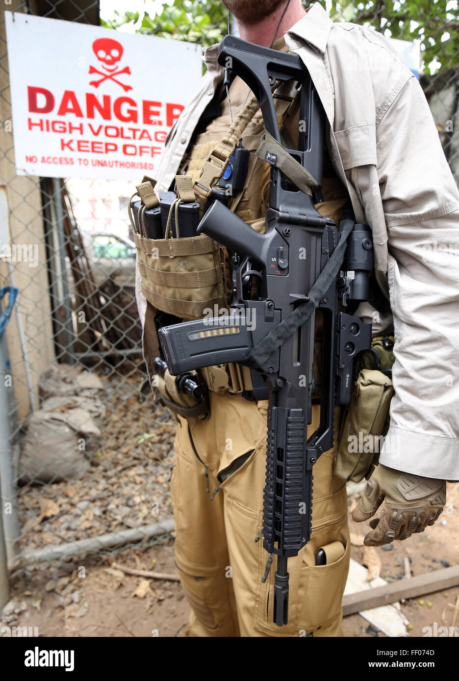 Un gardien de sécurité armé, debout devant un panneau "danger. Haute tension. Garder !", au cours d'une visite du président allemand Gauck, à Lagos au Nigeria, 9 février 2016. Le président Gauck est sur 5 jours au Nigéria. PHOTO : WOLFGANG KUMM/DPA Banque D'Images