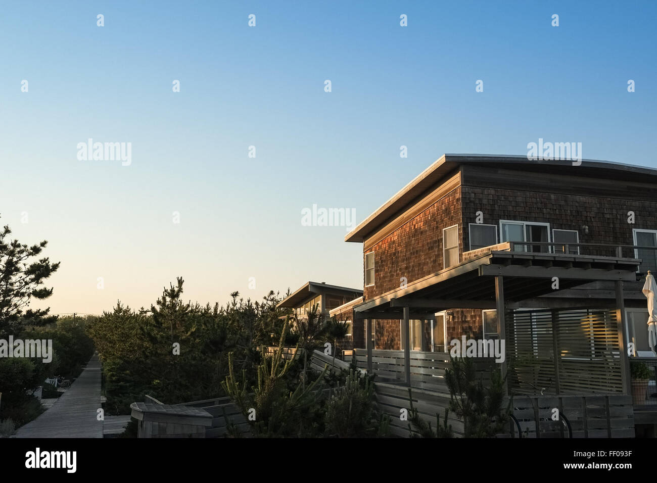 Une charmante maison de style bardeaux avec un fond de ciel bleu. Le style architectural comporte des bardeaux de bois à l'extérieur, un élément classique de ce design résidentiel américain. La maison comprend une terrasse et des plantes autour de l'extérieur. Banque D'Images