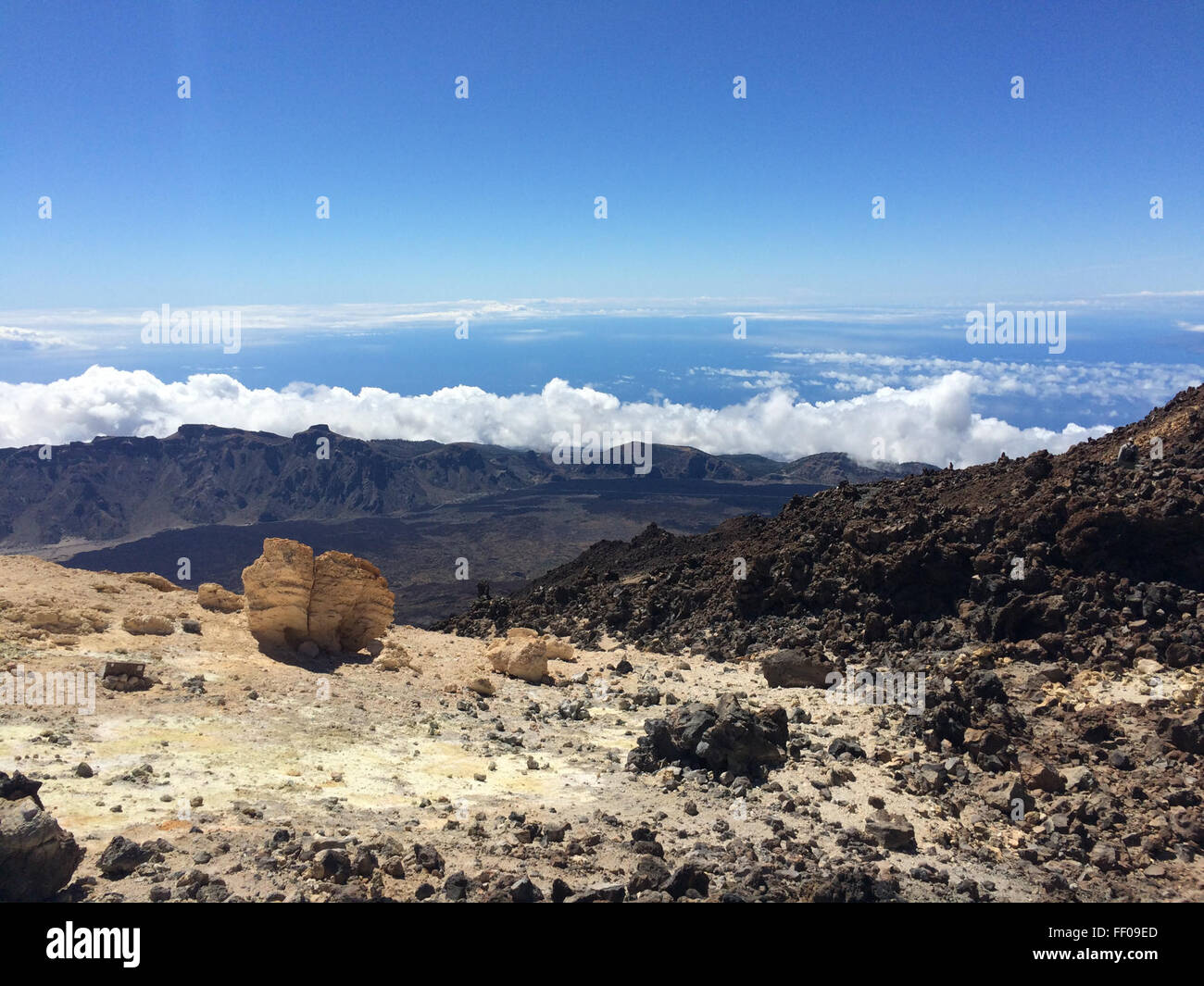 Une vue panoramique d'un sommet de montagne s'élevant au-dessus d'une mer de nuages, avec le ciel bleu clair et les nuages cumulus encadrant le paysage. Cette image capture la grandeur et la sérénité des vues en haute altitude, offrant une vue imprenable sur la beauté et la tranquillité de la nature. Banque D'Images