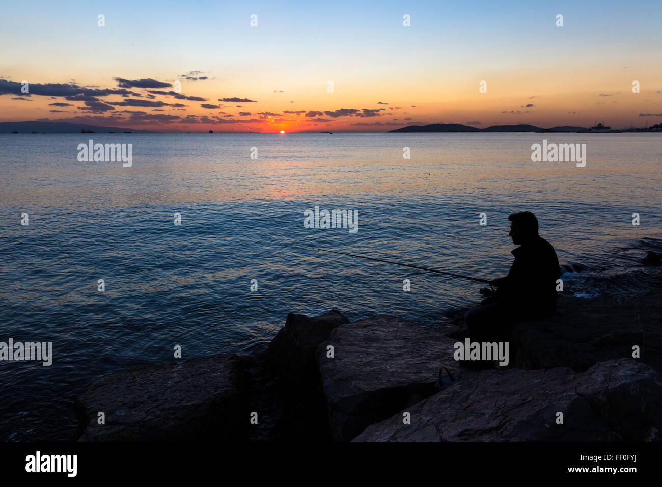 Vue panoramique du magnifique coucher de soleil avec une silhouette pêcheur assis sur les rochers près de seaside Banque D'Images