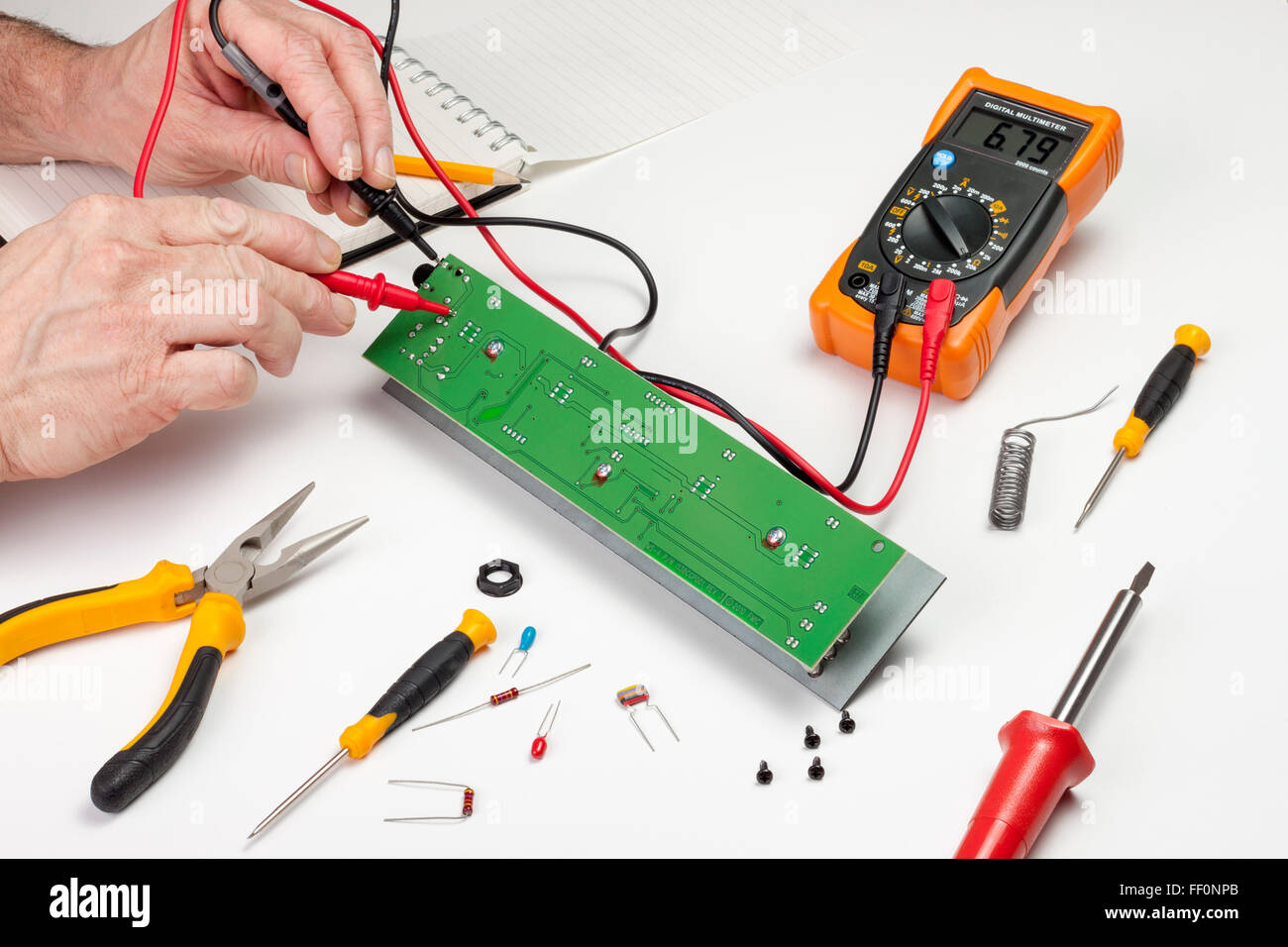 Ingénieur en électronique à son établi à l'aide d'un multimètre pour tester une carte à circuits imprimés Banque D'Images