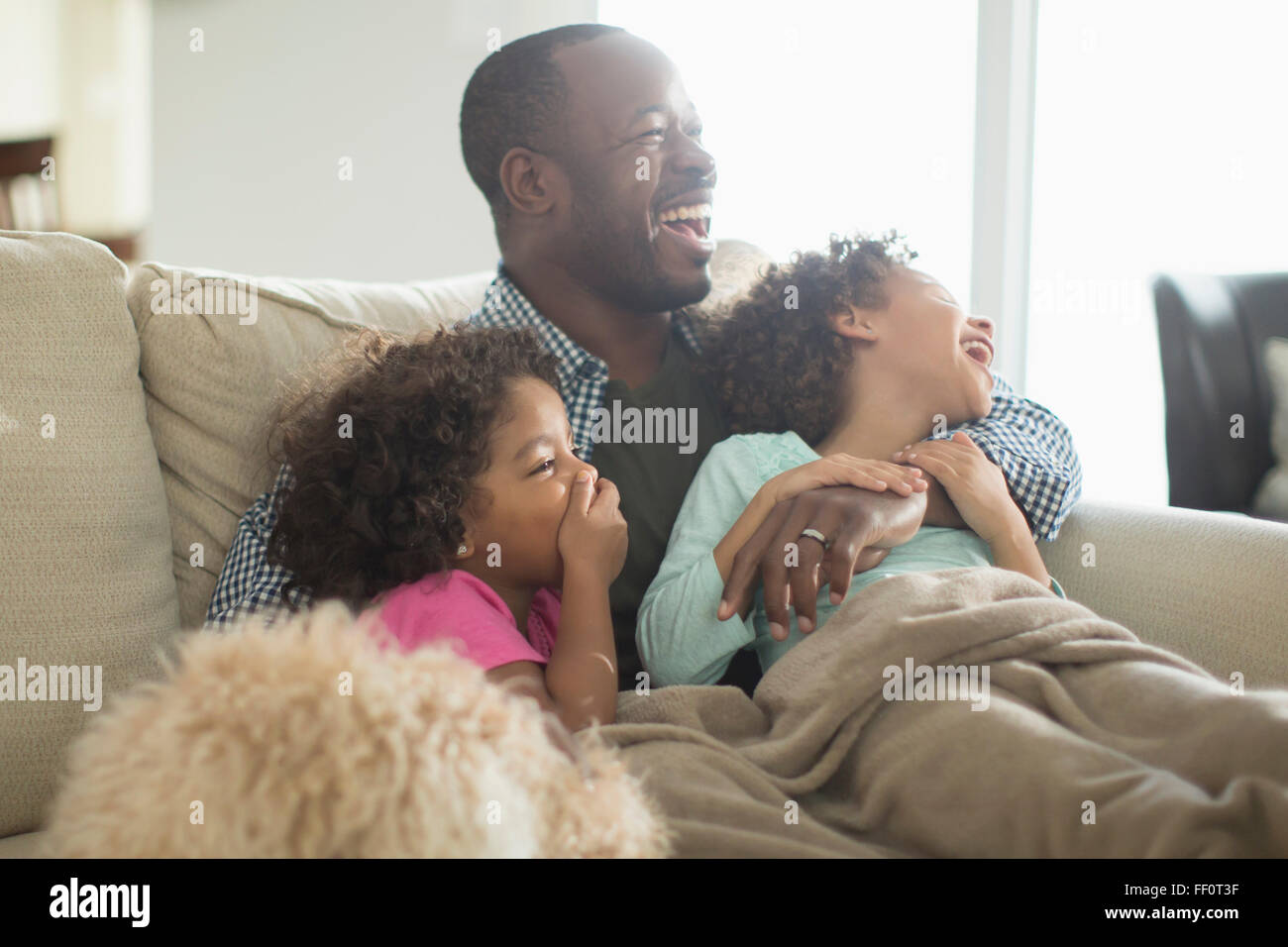 Père et filles à regarder la télévision sur le canapé Banque D'Images