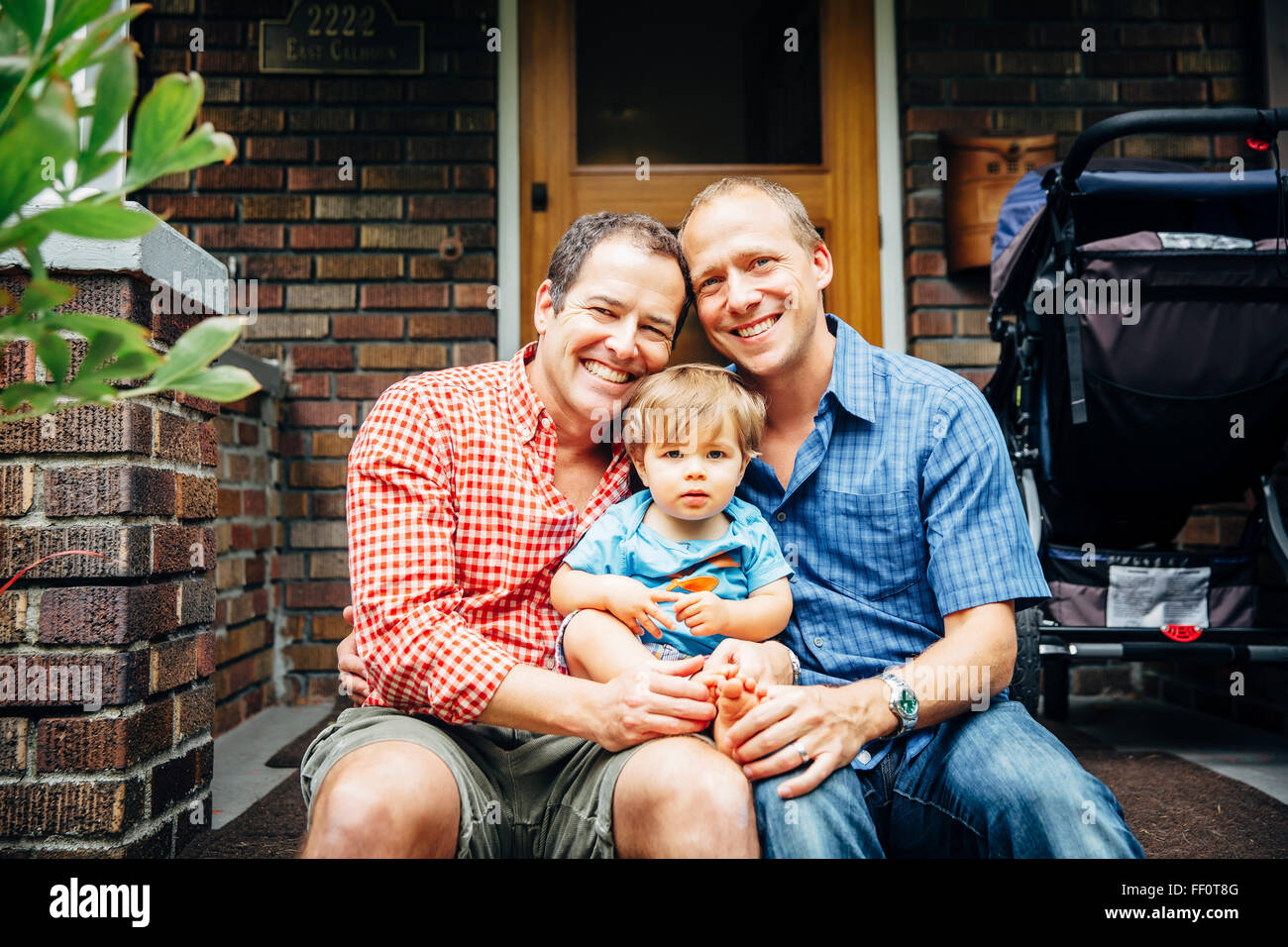 Les pères gays holding baby son sur avant stoop Banque D'Images
