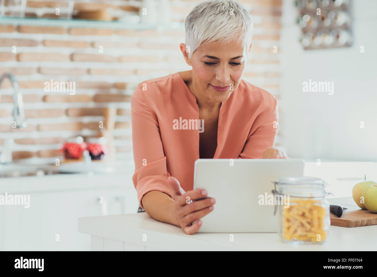 Older Caucasian woman using digital tablet in kitchen Banque D'Images