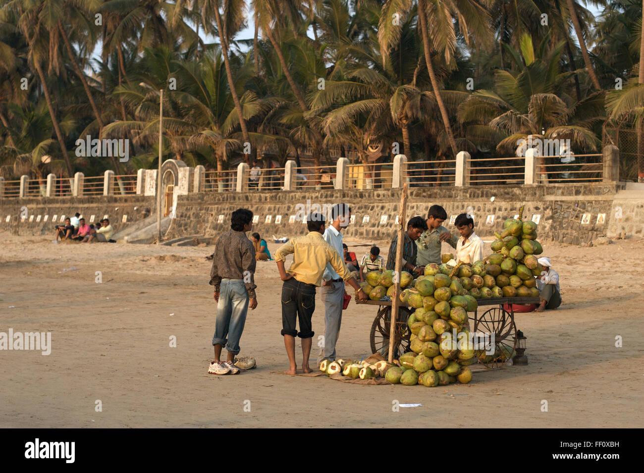 Un groupe de jeunes hommes se sont réunis autour d'un vendeur de noix de coco sur la plage de Juhu à Mumbai, Inde. Banque D'Images