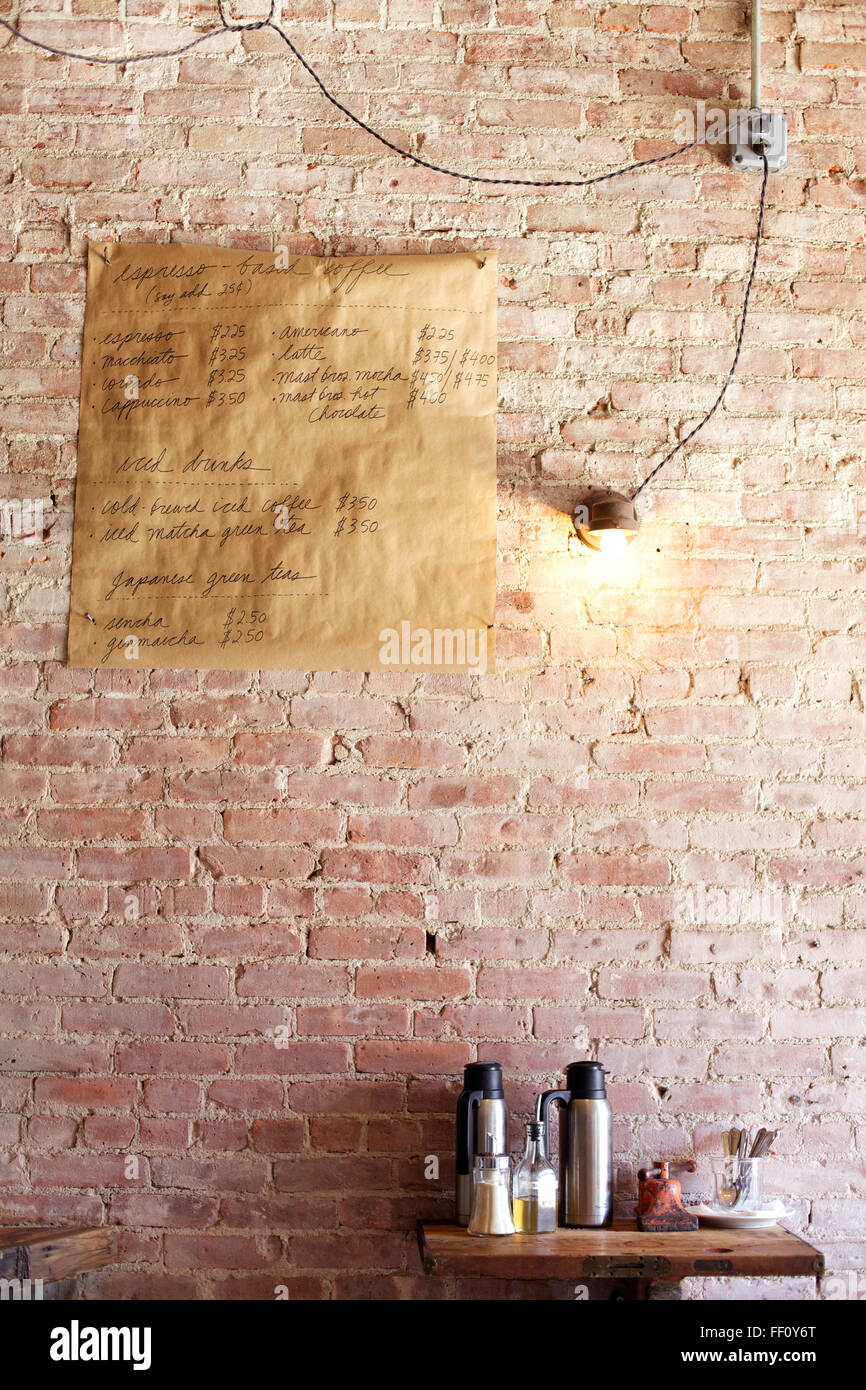 Un bar café menu accrochées sur un mur de brique au-dessus d'une crème et sucre gare éclairée par une seule ampoule nue. Banque D'Images