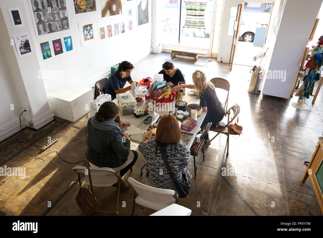 Cinq personnes assis autour d'une table avec des fournitures d'artisanat dans un espace ensoleillé lumineux, chacun travaillant sur son projet tranquillement. Banque D'Images