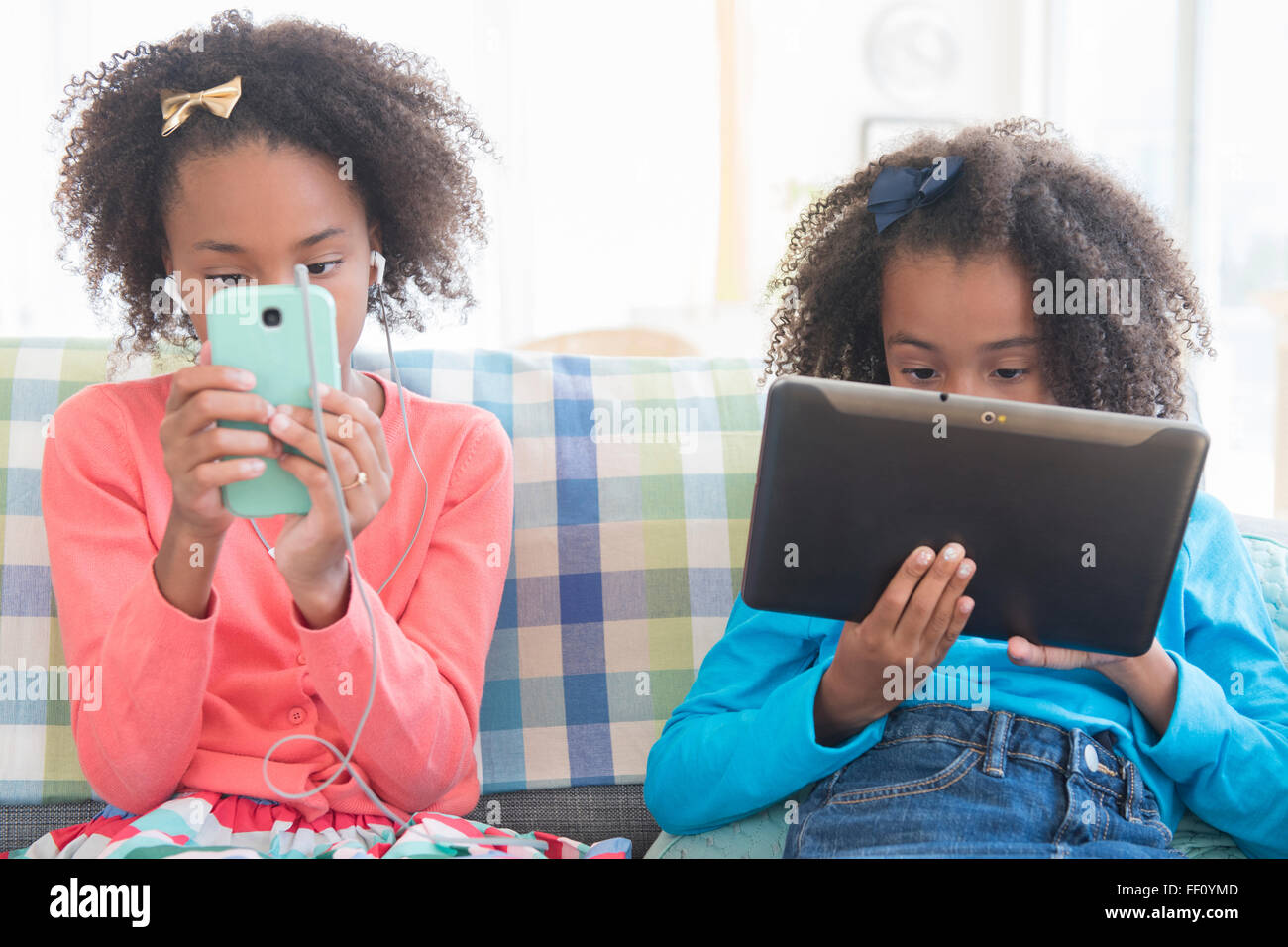 Mixed Race sisters en utilisant la technologie sur canapé Banque D'Images