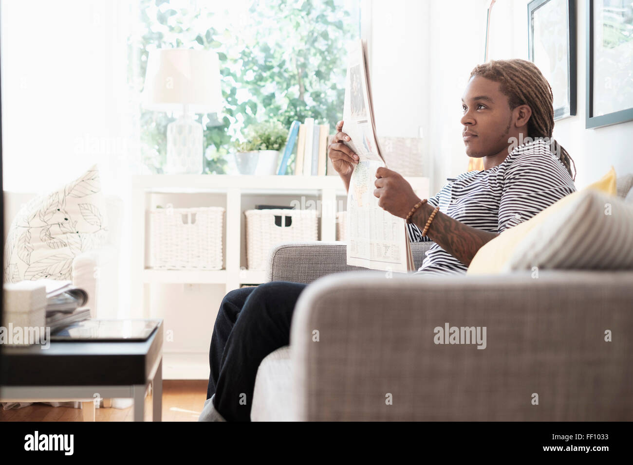 Mixed Race man reading newspaper on sofa Banque D'Images