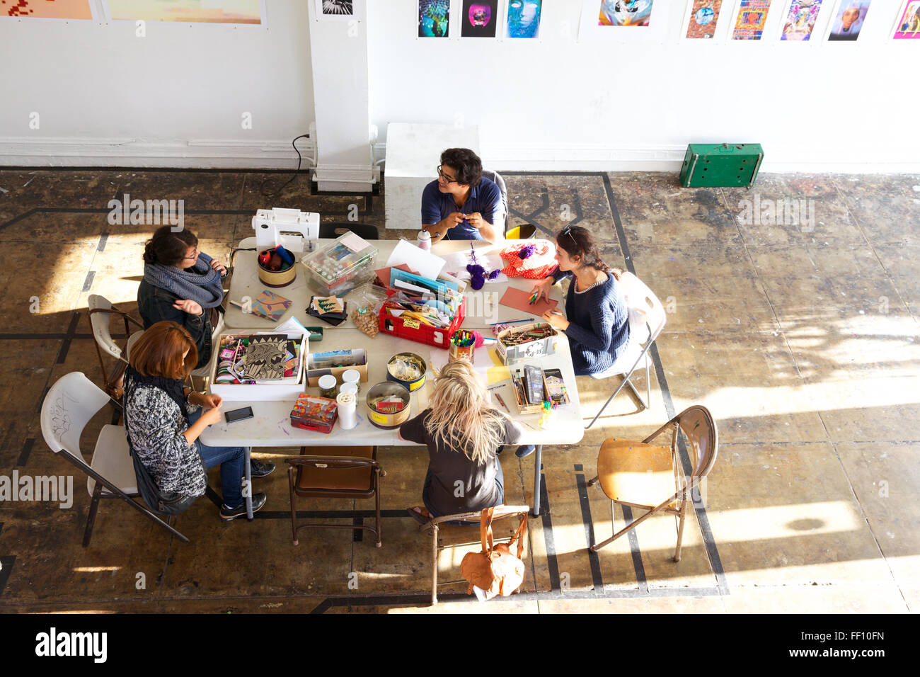 Cinq personnes assis autour d'une table avec des fournitures d'artisanat dans un espace ensoleillé lumineux, chacun travaillant sur son projet tranquillement. Banque D'Images