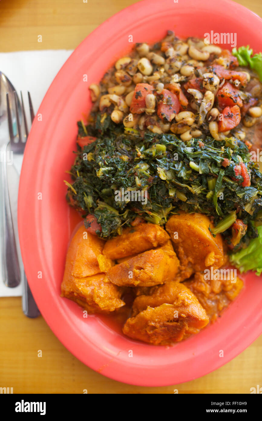Un repas sain de soul food végétalienne, Black Eyed Peas, verts et des patates douces servi sur une plaque lumineuse rose saumon, d'en haut. Banque D'Images