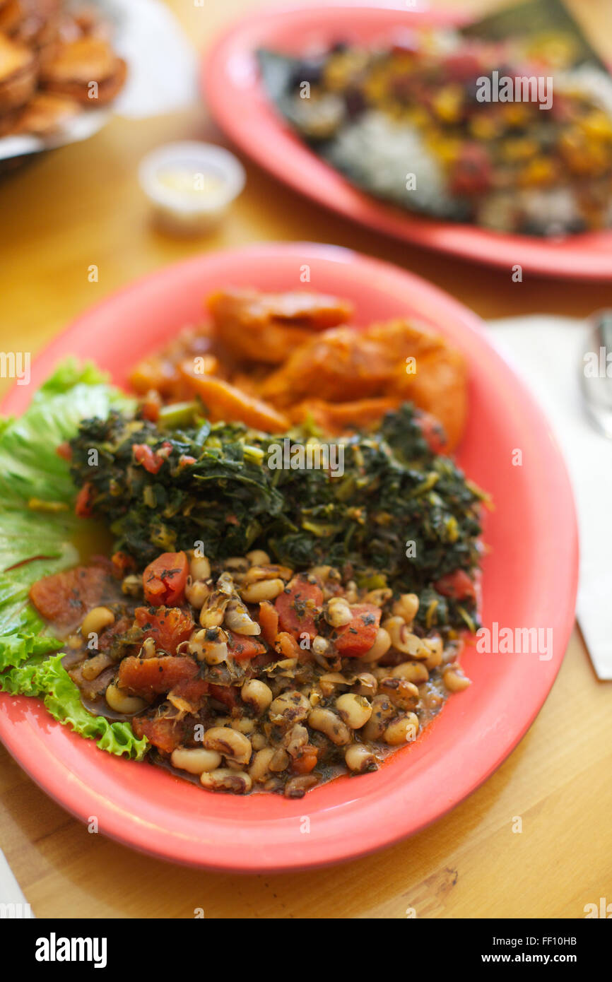 Un repas sain de soul food vegan y compris Black Eyed Peas et verts servi sur une plaque lumineuse rose saumon, angle de 45 degrés. Banque D'Images