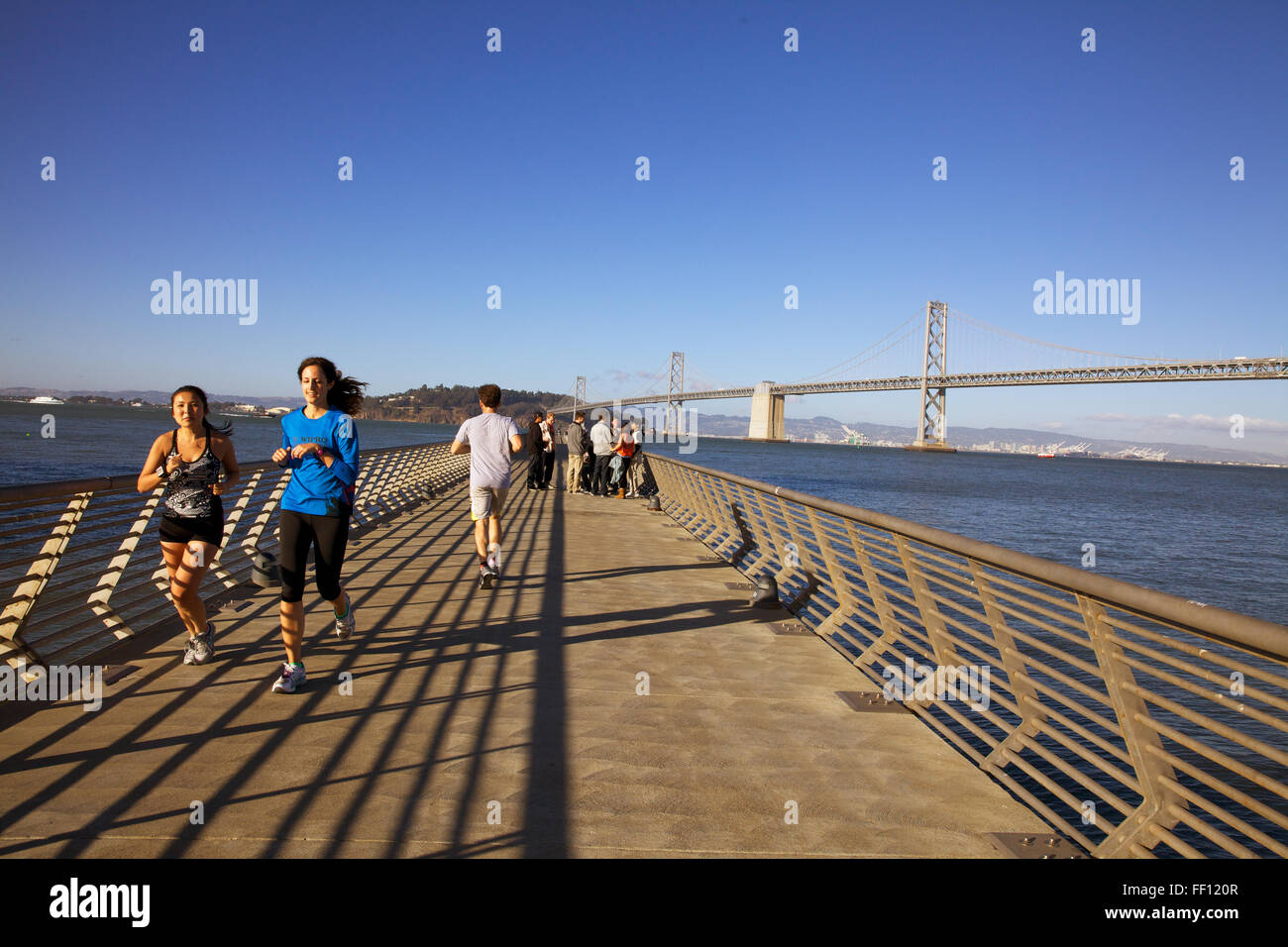 Les gens du jogging le long du Pier 14 San Francisco sur un après-midi ensoleillé avec le Bay Bridge dans le fond. Banque D'Images