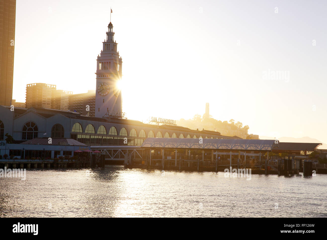 San Francisco Ferry Building sur l'Embarcadero avec le soleil qui brille derrière la tour de l'horloge a photographié de l'eau. Banque D'Images