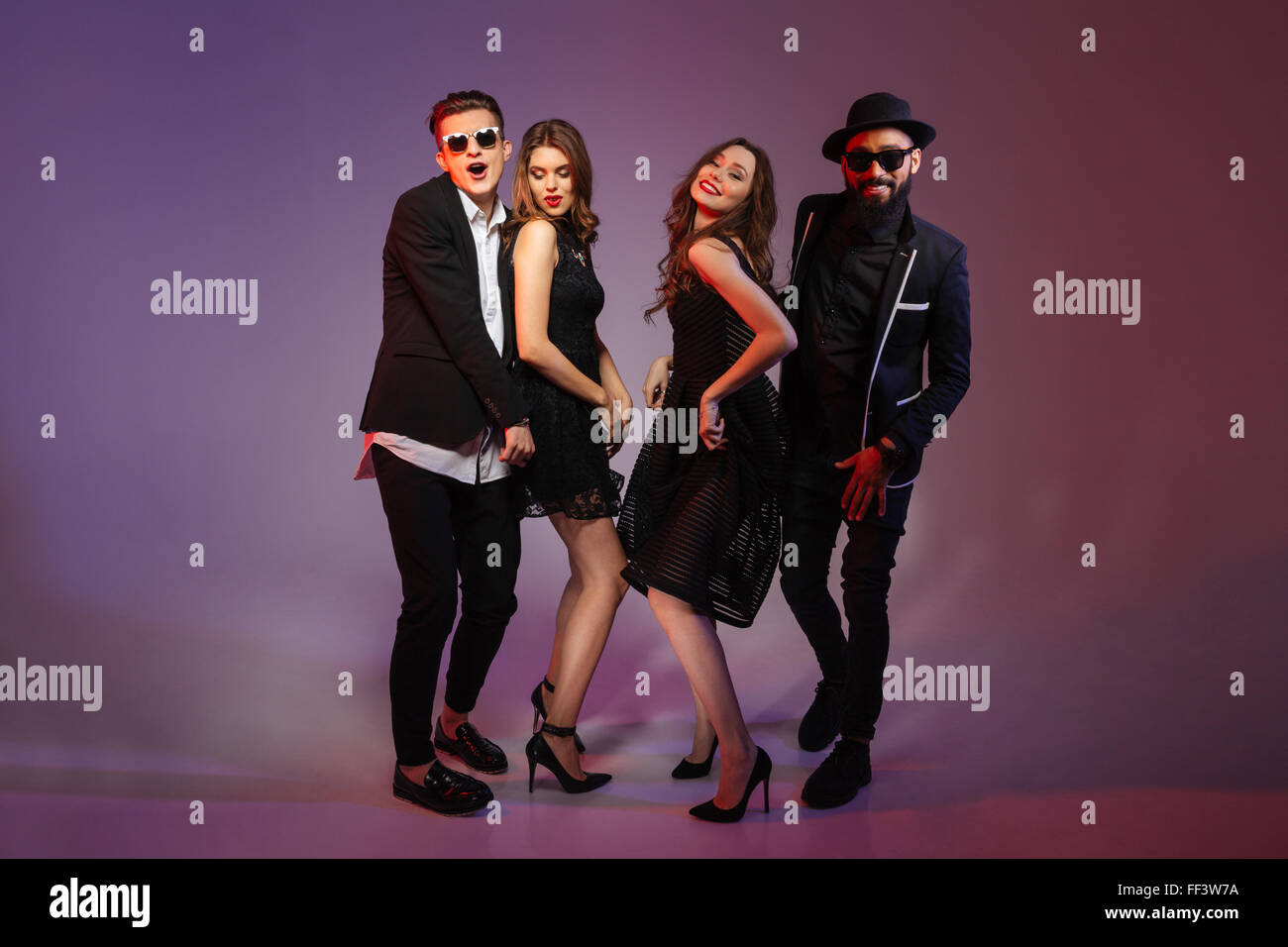 Toute la longueur de deux couples de jeunes gens heureux danser sur fond violet Banque D'Images