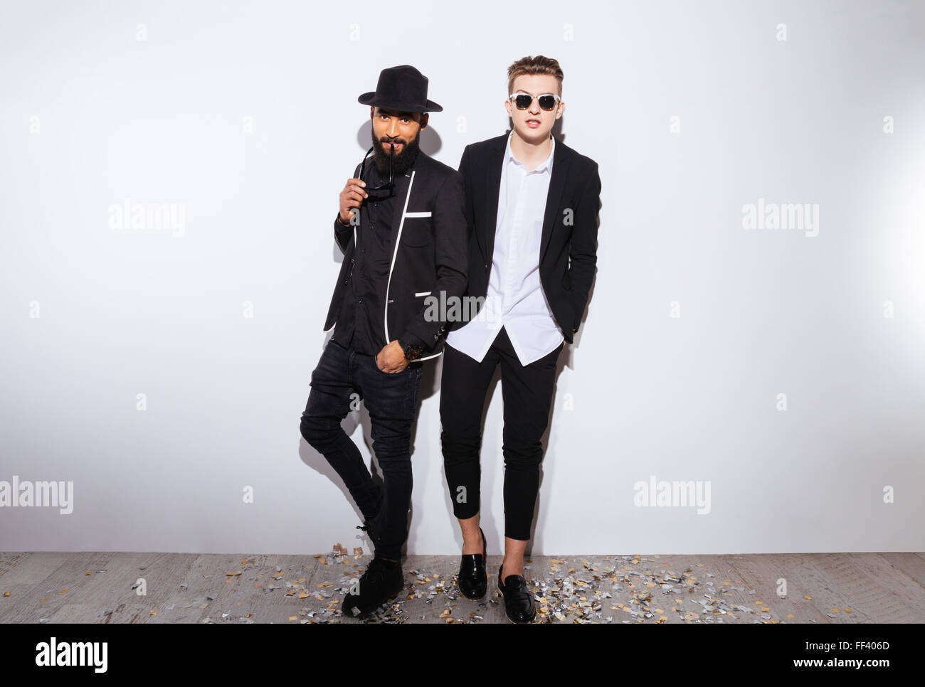 Deux beaux jeunes hommes confiants en costumes noirs modernes debout sur fond blanc Banque D'Images