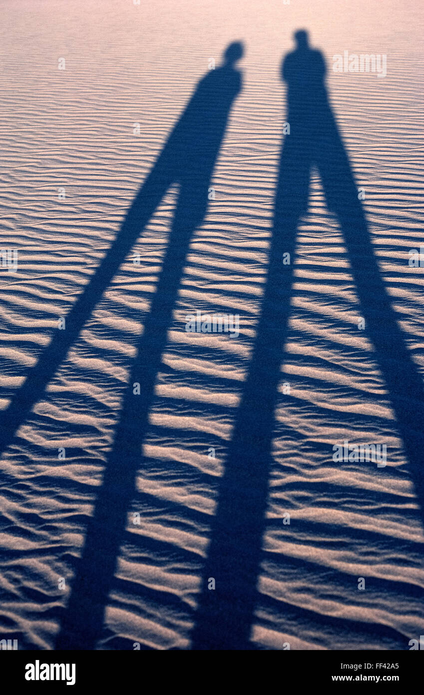 Le soleil couchant jette les grandes ombres de deux visiteurs de marcher à travers le vent-ridée dunes près de Stovepipe Wells dans Death Valley National Park en Californie, USA. La géographie de ce vaste parc s'étend de ces sables du désert de badlands colorés, robustes, canyons et montagnes enneigées. Certaines des plus chaudes de l'enregistrement des températures dans le monde, la vallée de la mort est à la hauteur de son nom d'interdiction. Banque D'Images
