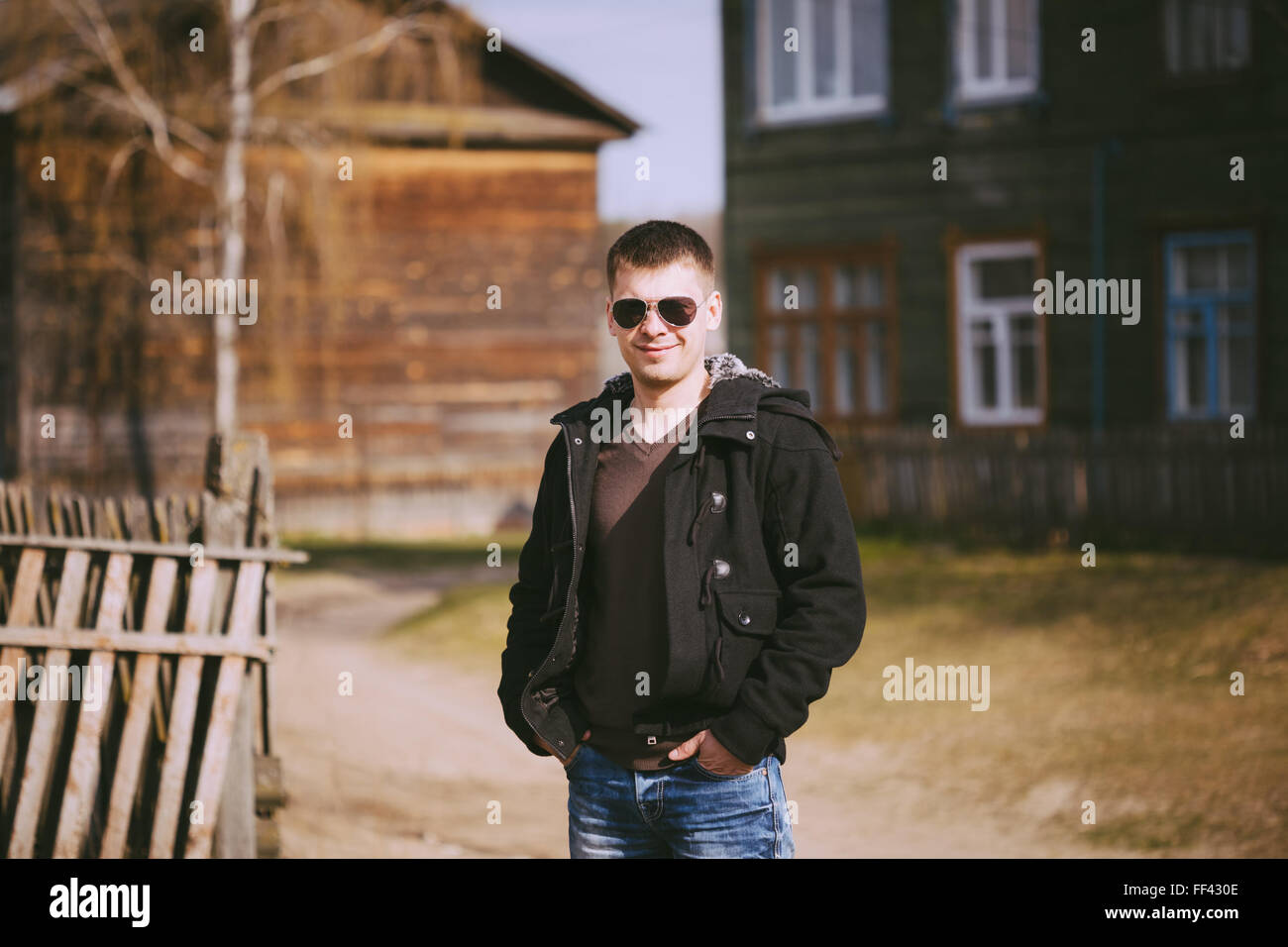 Beau jeune homme d'un séjour près de vieille maison de bois dans la journée d'automne, de détente, de réflexion, de sourire. Style Casual - jeans, veste, Sung Banque D'Images