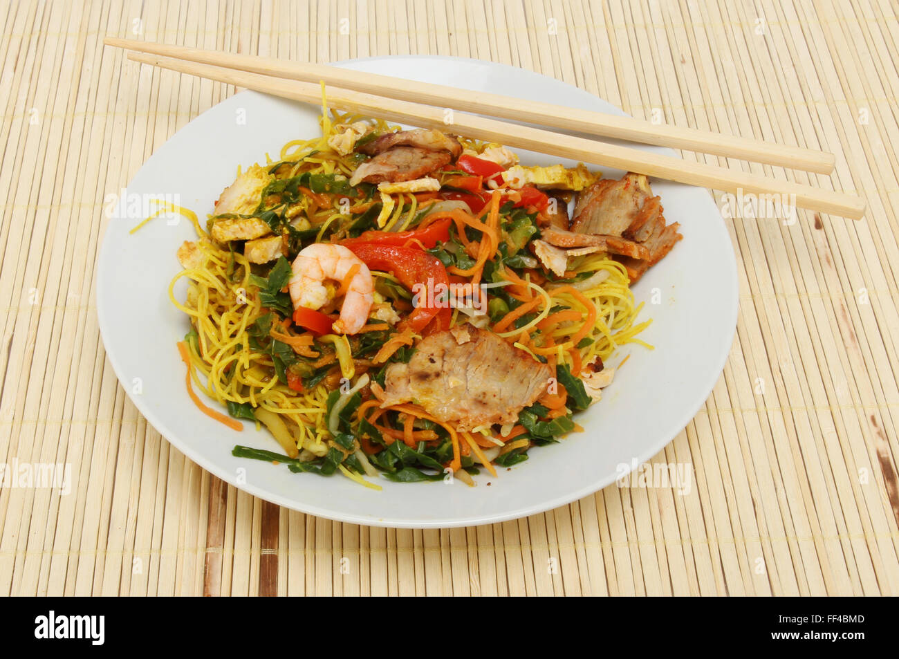 Singapour nouilles dans un bol avec des baguettes sur un tapis de bambou Banque D'Images