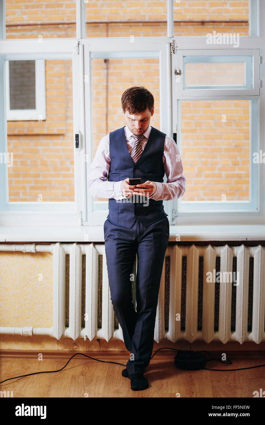 Handsome Man en tenue d'affaires séjournant dans la chambre près de la fenêtre et Holding Mobile Phone Banque D'Images