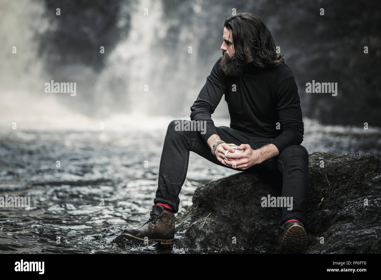 Un homme assis par un jet d'eau qui coule sur les rochers. Banque D'Images