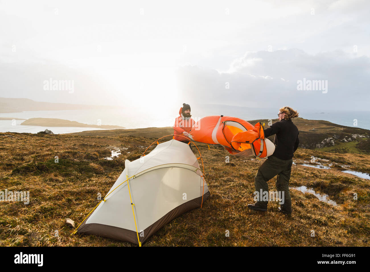 Deux hommes tenant et de mettre en place une petite tente en espace ouvert. Camping sauvage. Banque D'Images