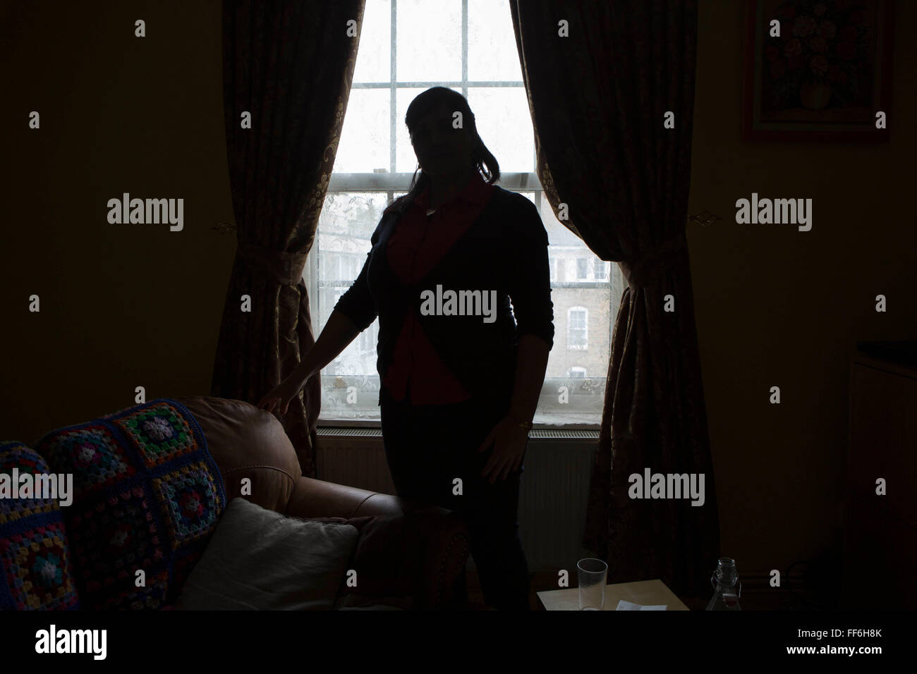Une dame non identifiée est silhouetté devant sa fenêtre du salon. L'isolement et les problèmes de santé mentale à Londres, au Royaume-Uni. Banque D'Images