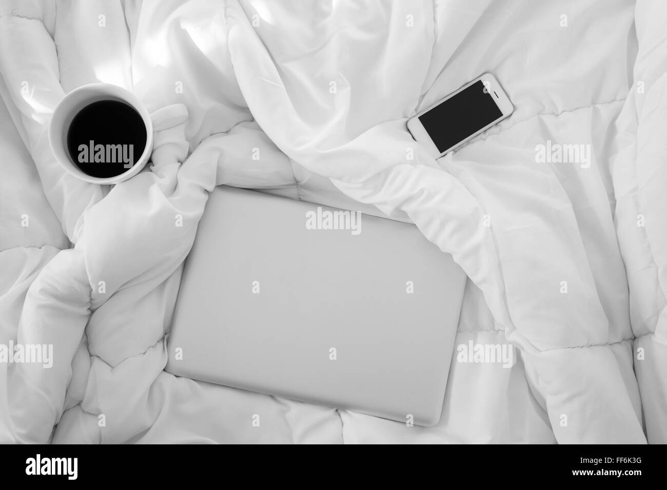 Travailler au lit , portable, smartphone et blanc tasse de café sur le lit blanc, la lumière du matin Banque D'Images