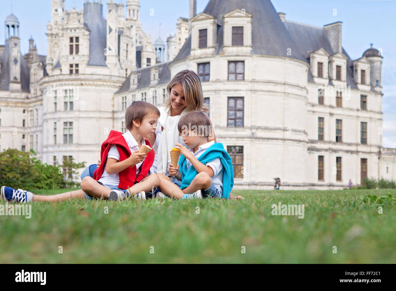 Deux adorables garçons et maman de vêtements, la consommation de crème glacée assis sur une pelouse en face de la plus grand château le long de la Loire Banque D'Images