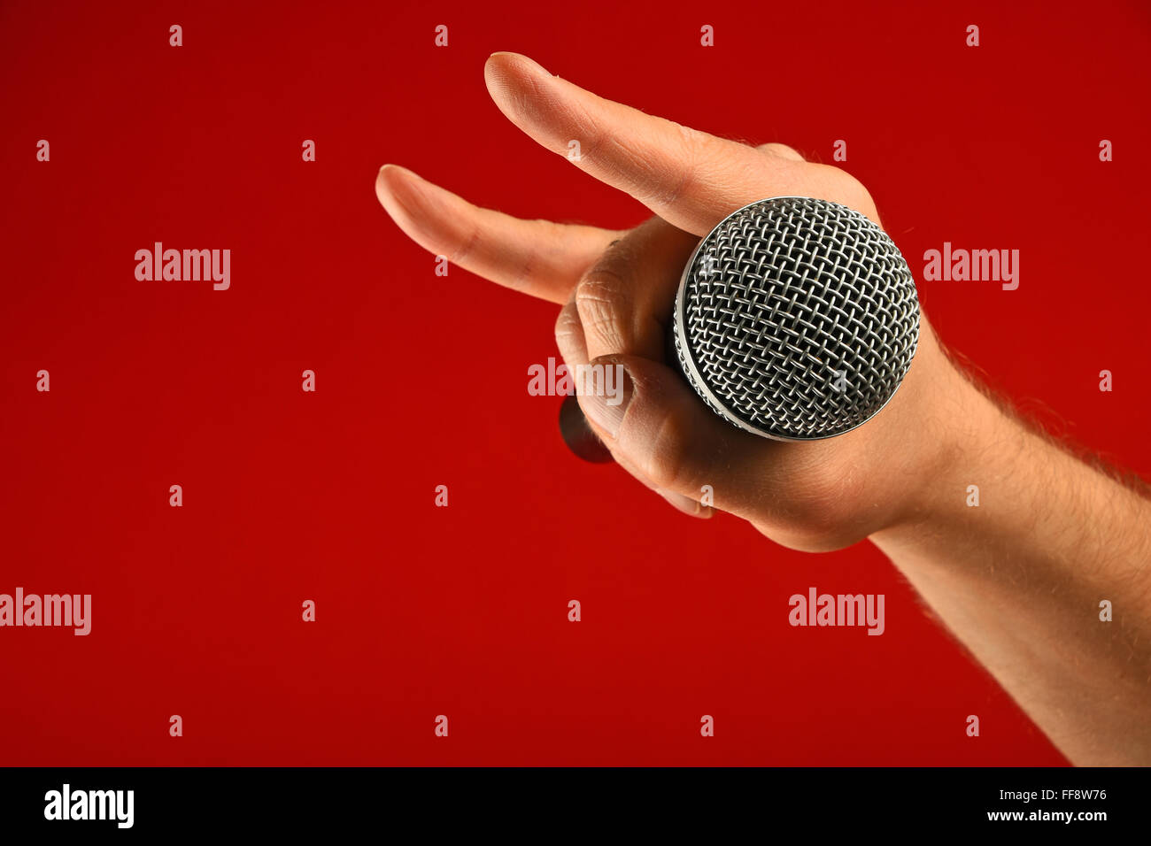Man hand holding microphone vocal avec des cornes de diable geste rock metal sign sur fond rouge, side view Banque D'Images
