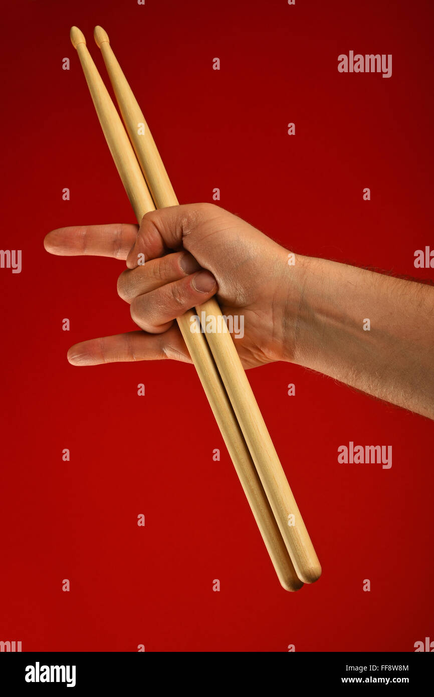 Man main tenant deux baguettes avec des cornes de diable geste rock metal sign sur fond rouge Banque D'Images